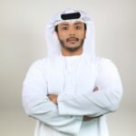 Young Middle Eastern man in white thobe standing confidently indoors.